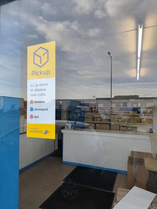 Livreur souriant en uniforme bleu et casquette jaune tenant un colis, debout près d'un chronomètre géant et de cartons empilés sur fond turquoise dégradé