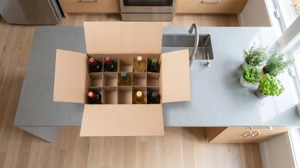 Cinq bouteilles de vin alignées sur surface claire avec emballages cylindriques en carton kraft brun, bouchons en liège disposés devant chaque bouteille